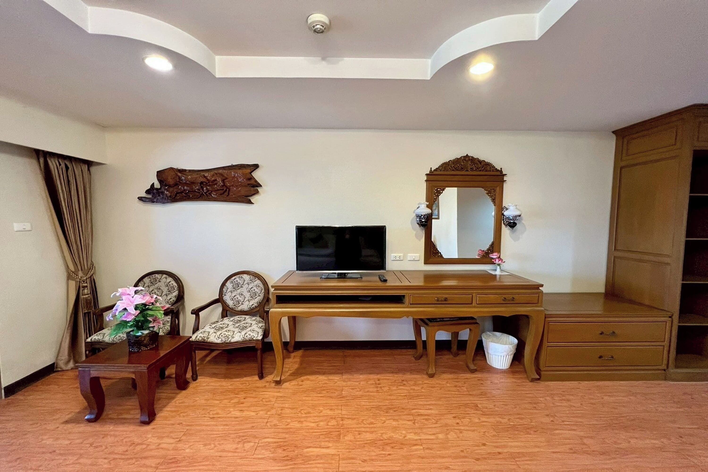 A room with a wooden desk, a television, a mirror, and two chairs.