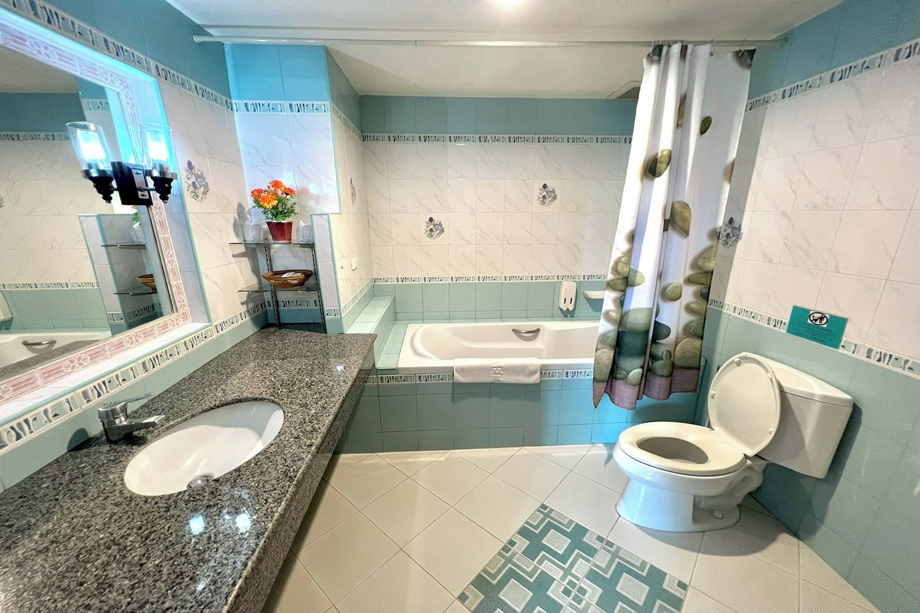 A bathroom with a granite sink, a bathtub, a toilet, and a mirror.