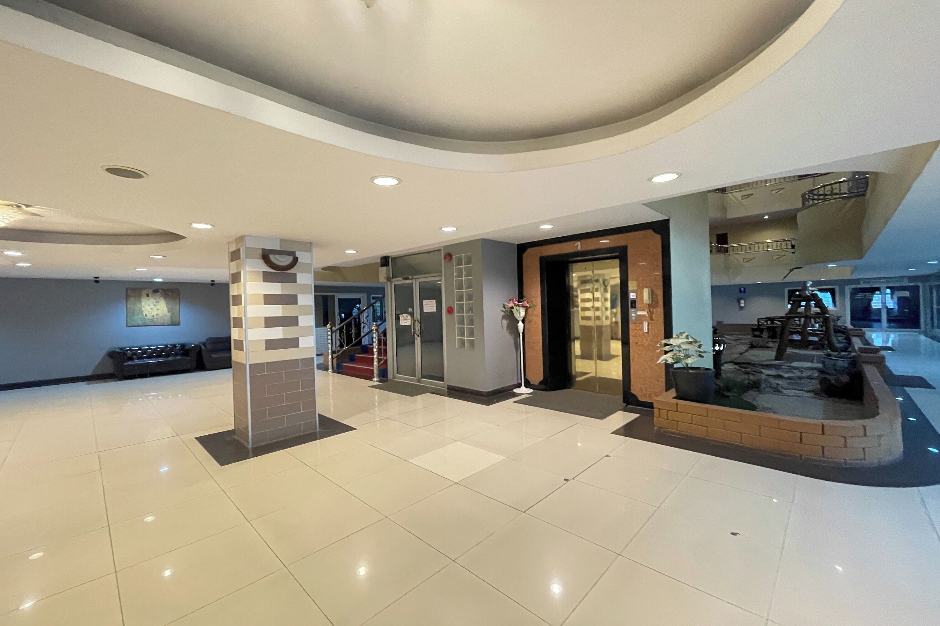 A spacious lobby with a tiled floor, a reception desk, a staircase, and a small indoor garden.