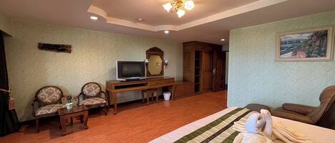 Habitación de hotel con una cama, dos sillones, un escritorio con televisor, un armario de madera y un cuadro en la pared.