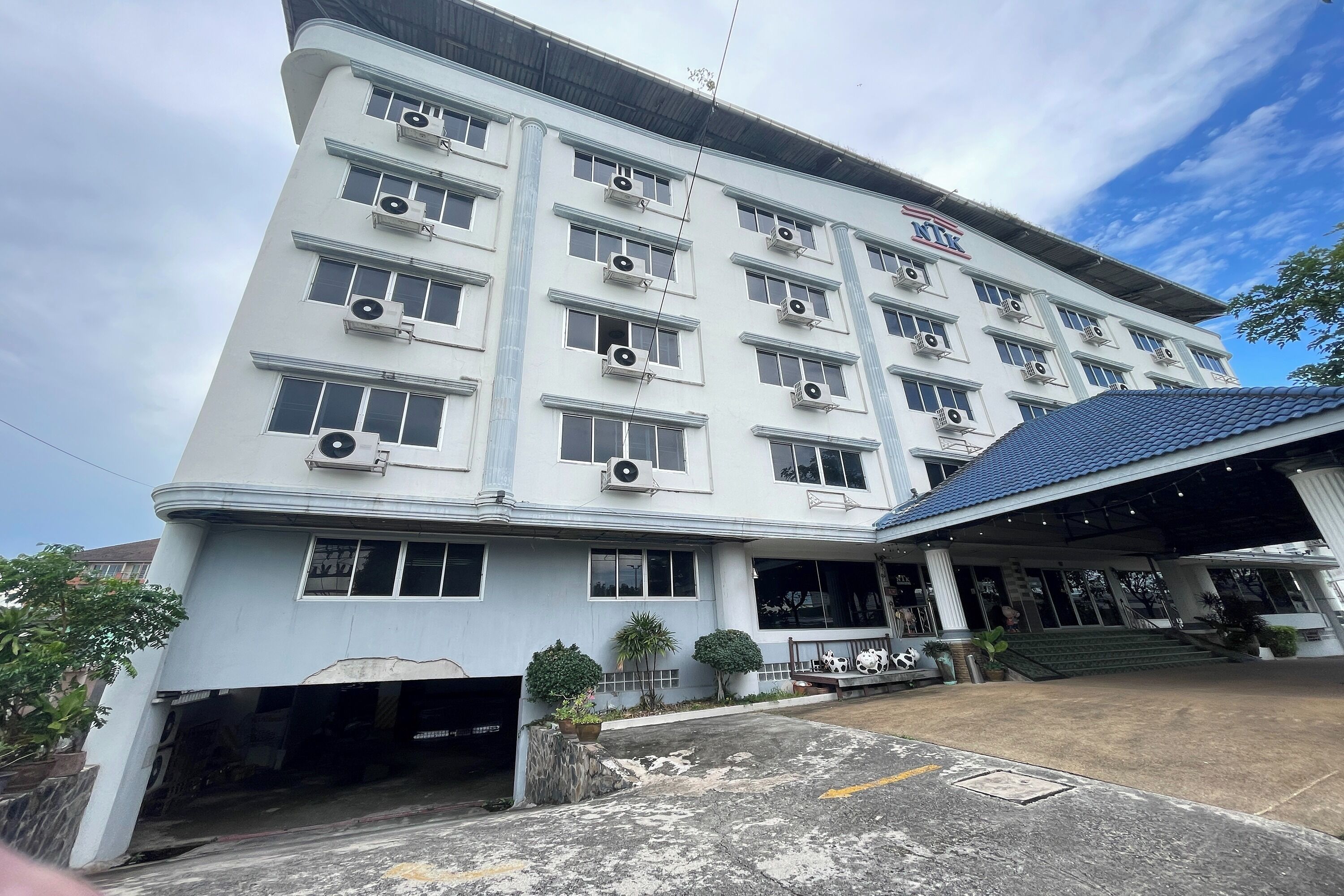 A multi-story building with air conditioning units, a covered entrance, and a parking area.