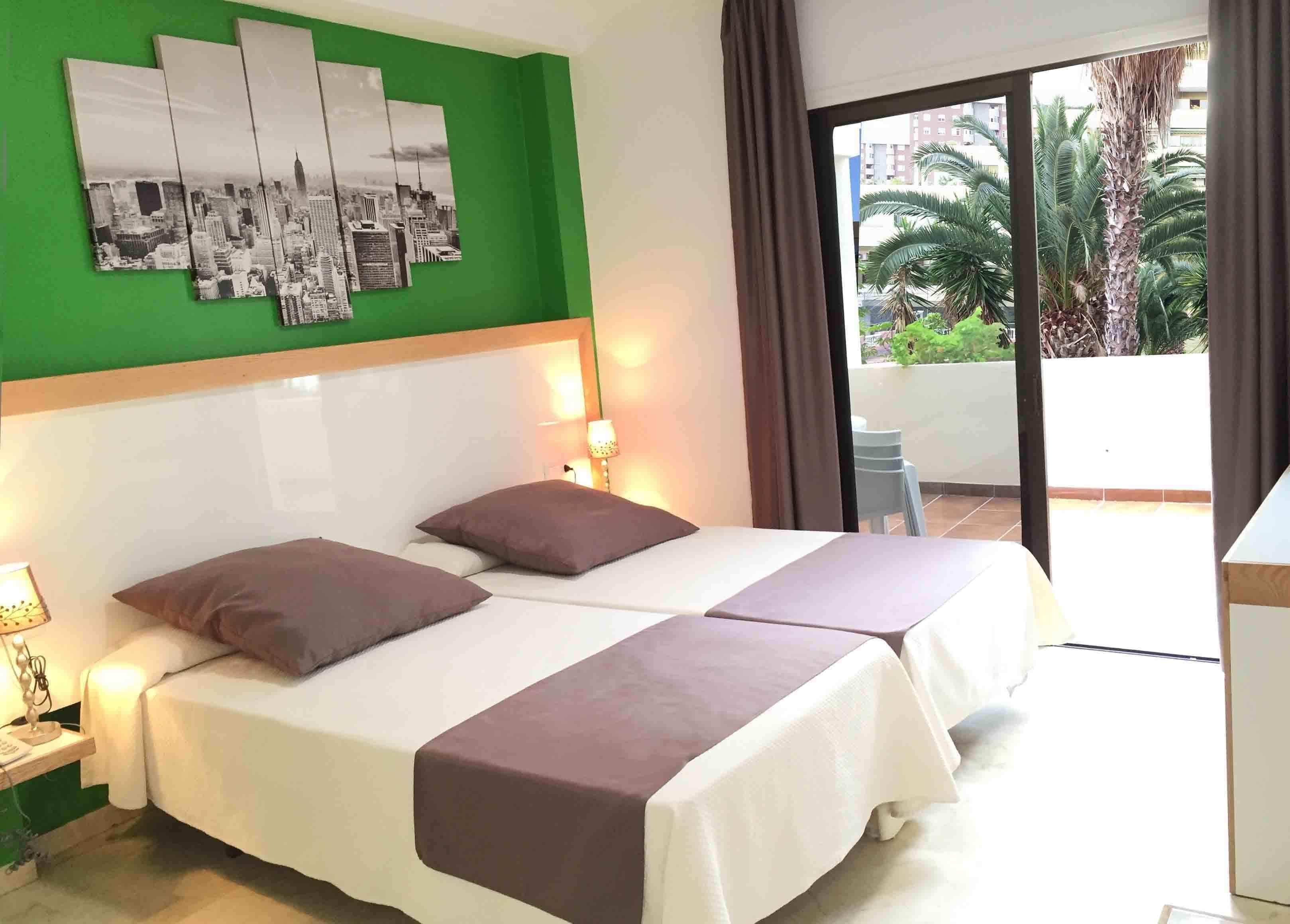 Habitación de hotel con una cama, pared verde y un cuadro con vistas a la ciudad.