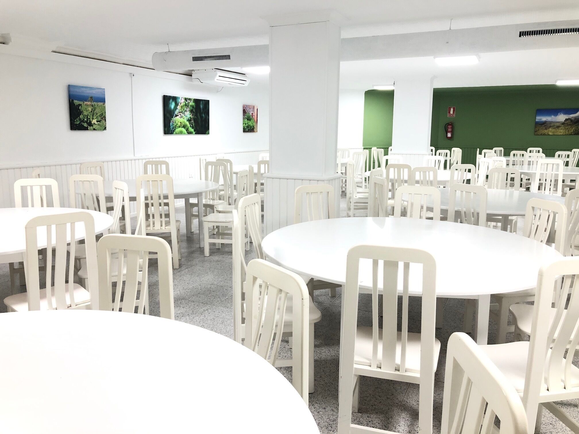 Une salle de conférence avec des tables et des chaises blanches, un mur d’accent vert et des tableaux encadrés accrochés au mur.