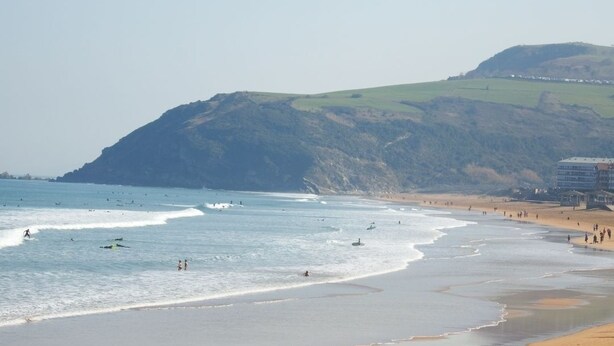 A beach with waves, a sandy shore, and a hill in the background. - Zarautz Beachside Surf Camp (Zarautz)