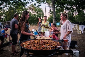Un grupo de personas reunidas alrededor de una zona de cocina al aire libre con una sartén de comida.