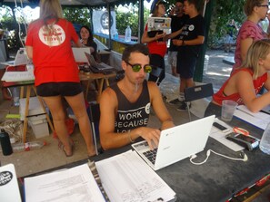 Un grupo de personas en un evento al aire libre, con computadoras portátiles y documentos sobre las mesas.
