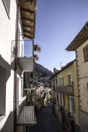 A narrow street with buildings on either side, featuring balconies and a mountain in the background. - Le Petit Fenestrelle (Fenestrelle)