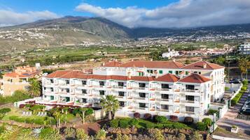 Hotel de diverses plantes amb teulada vermella, parets blanques i balcons. Està envoltat de vegetació i ofereix vista a un paisatge de muntanyes al fons.