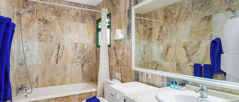 A bathroom with a marble wall, a bathtub, a toilet, a washing machine, and a sink.