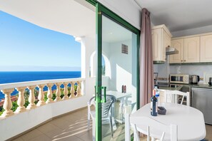 Ein Balkon mit Meerblick, ein Essbereich mit Tisch und Stühlen sowie eine Küchenzeile mit Schränken und Geräten.