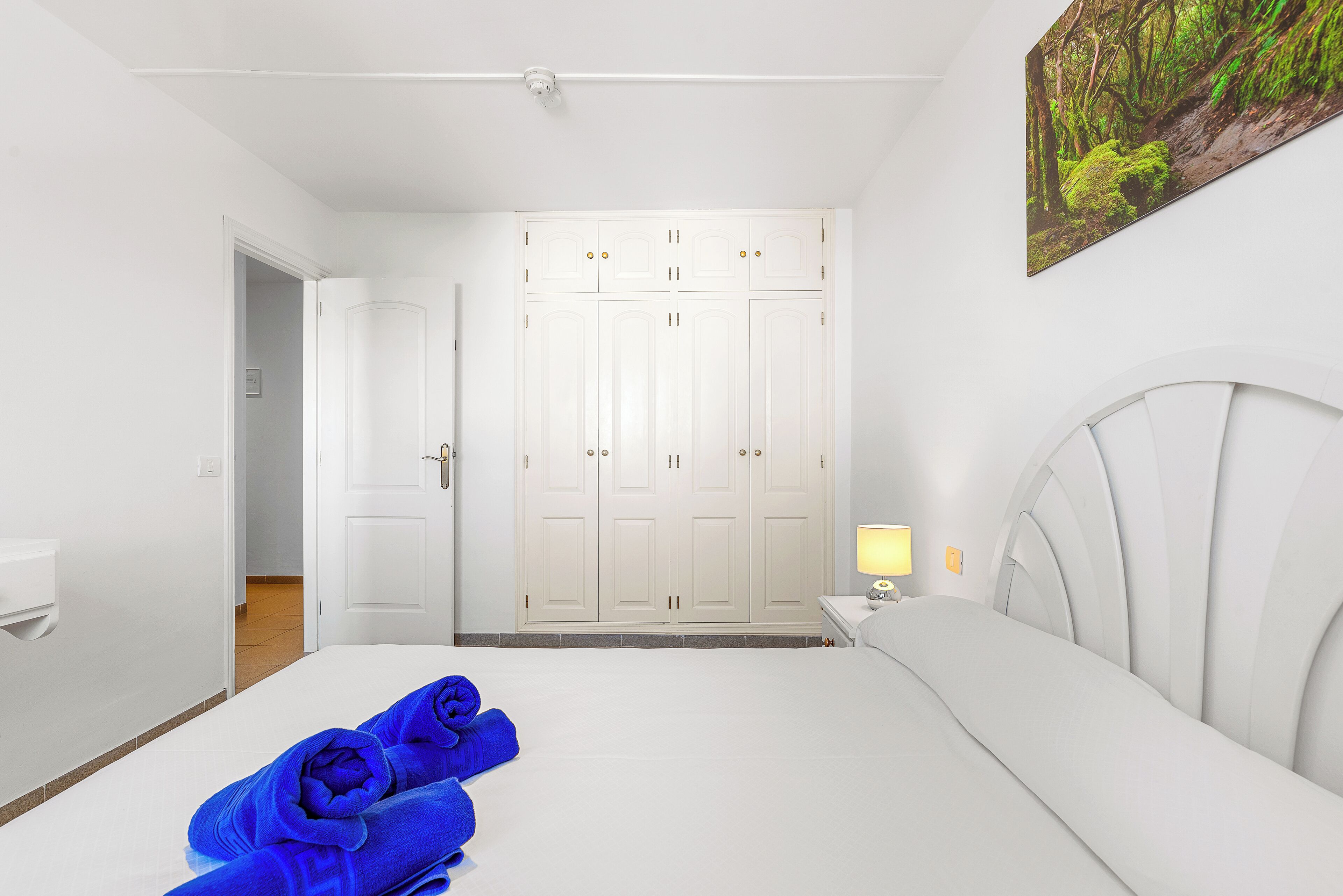 A hotel room with a bed, a nightstand, a lamp, and a wardrobe.