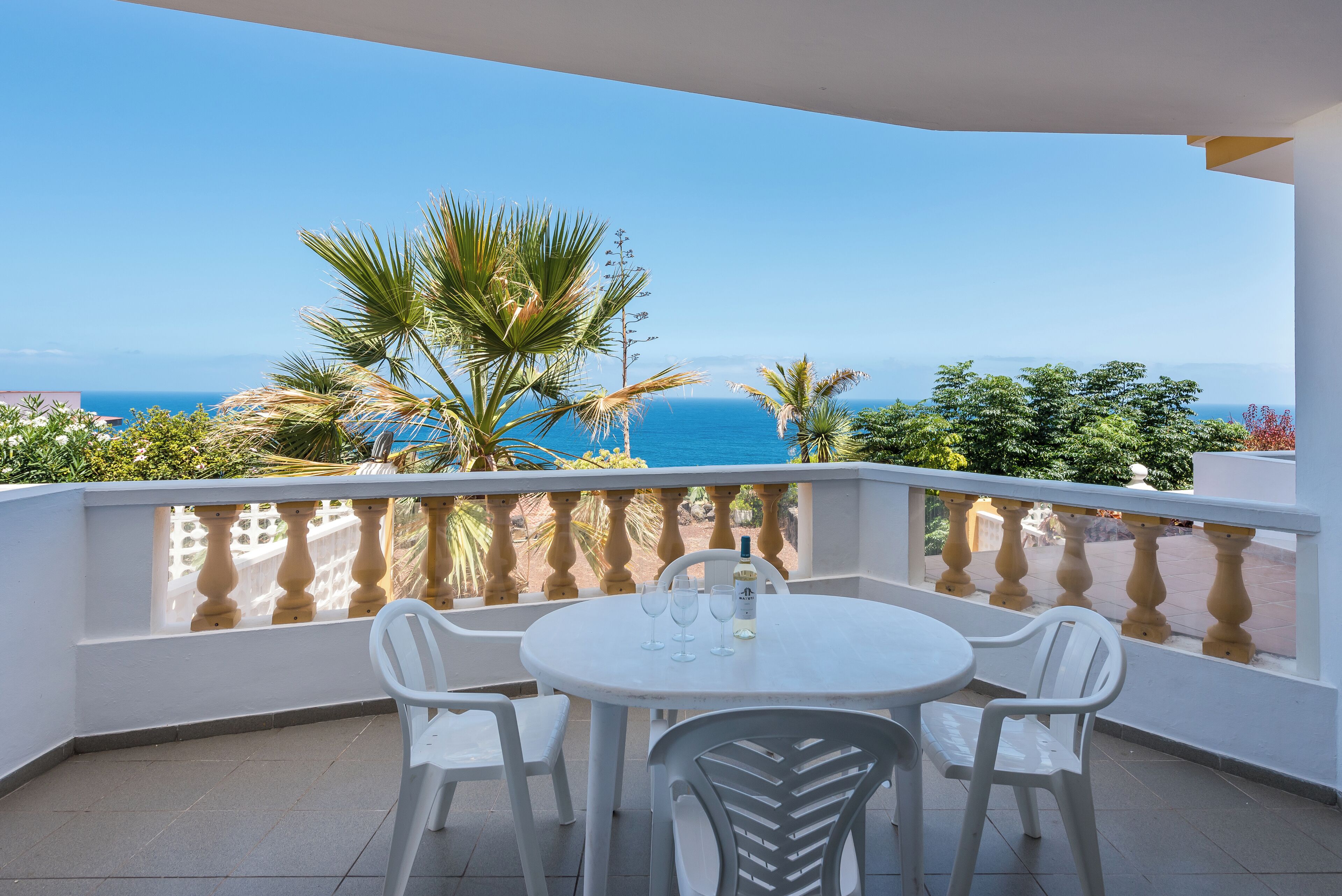 A balcony with a white table and chairs, a bottle of water, and a view of the ocean.