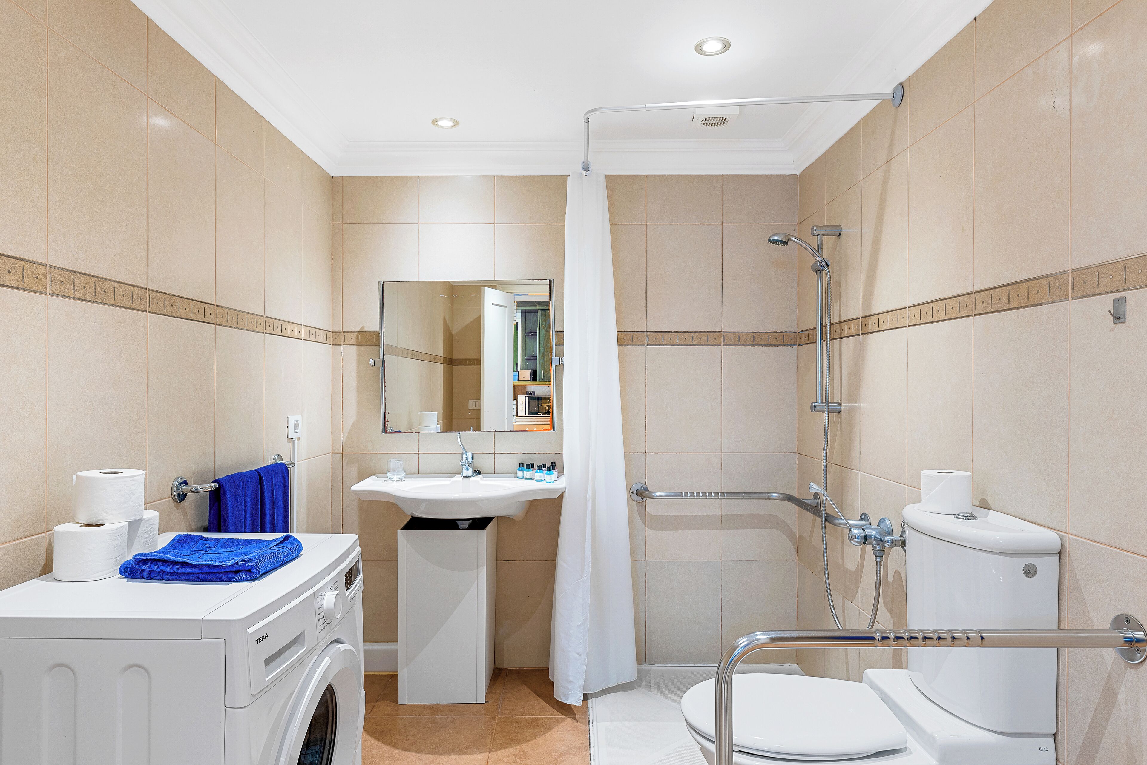 Une salle de bain d’hôtel de taille réduite, équipée d’un lave-linge, d’un lavabo, de toilettes et d’un espace douche.