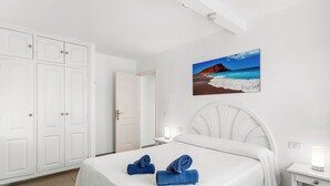 Ett hotellrum med en säng, vita gardiner, en tavla som föreställer en strand och ett nattduksbord med en lampa.