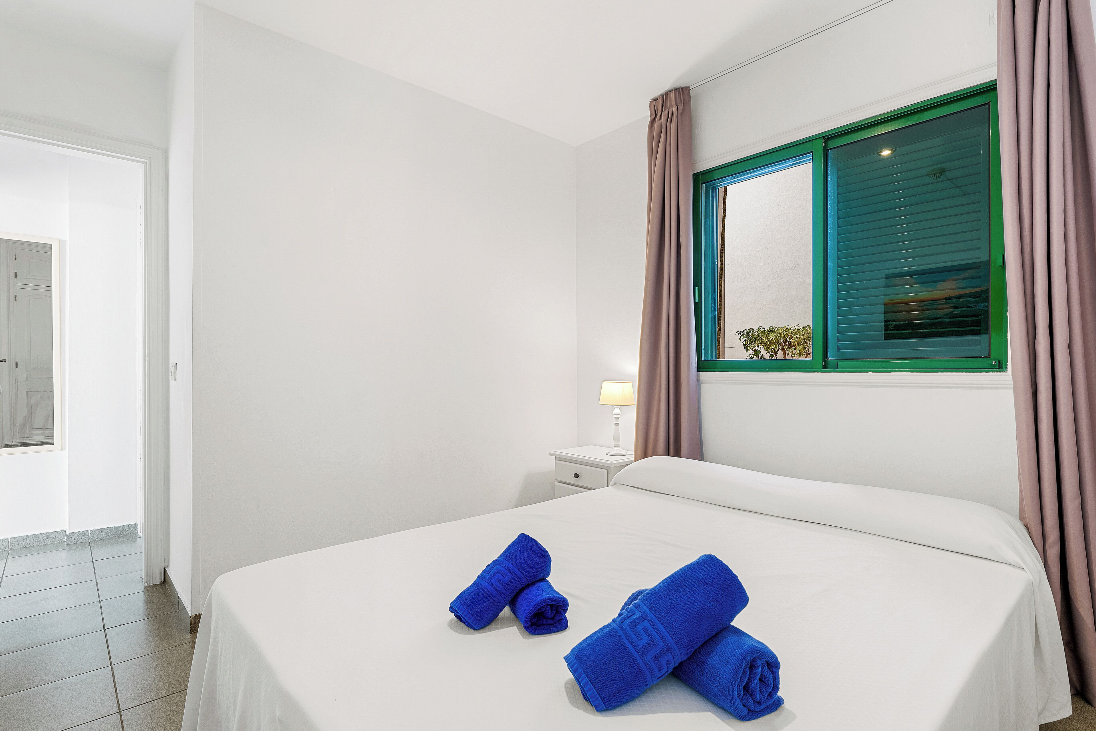A hotel room with a bed, a nightstand, a lamp, and a window with curtains.