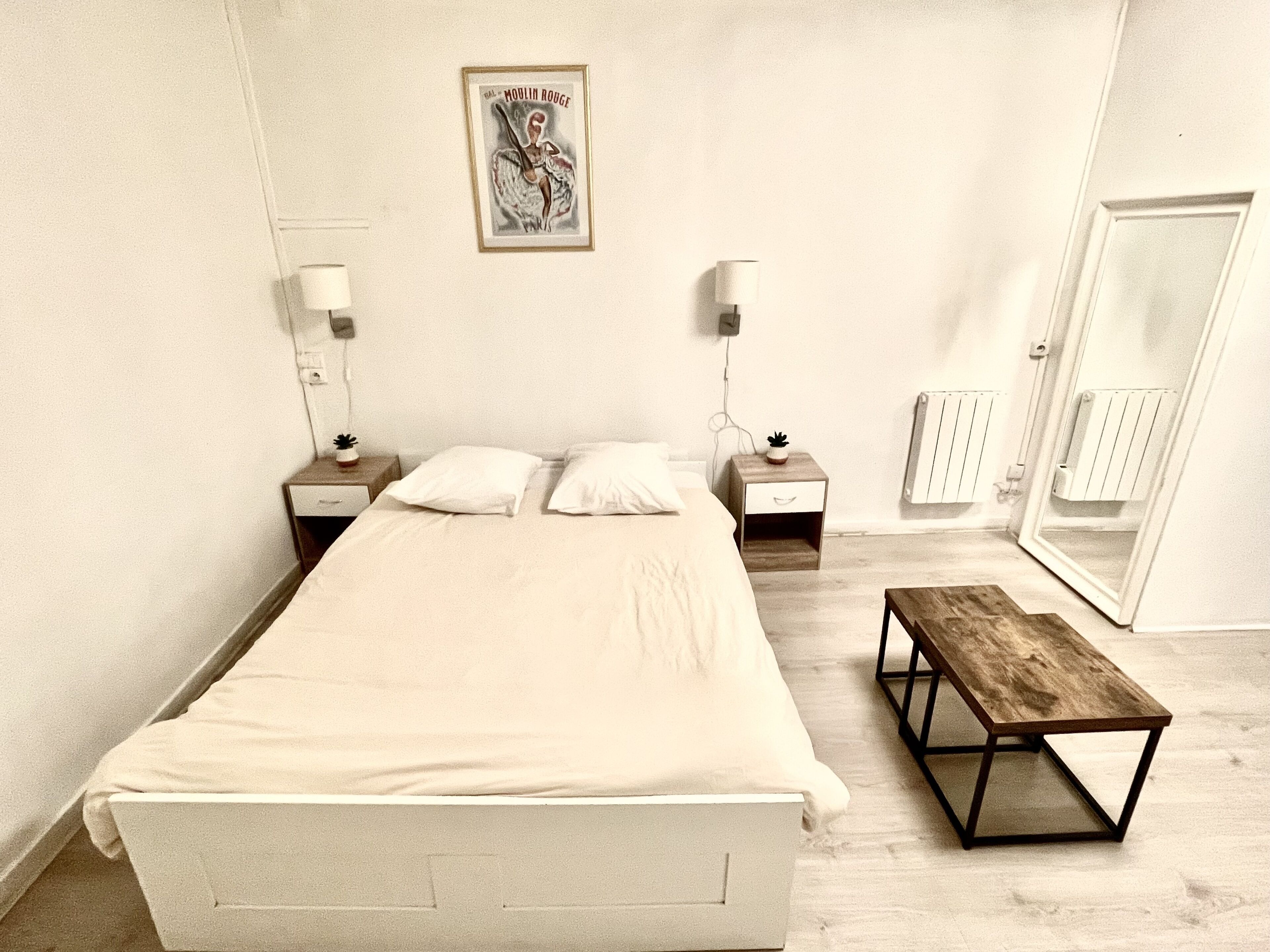 Ein schlicht eingerichtetes Schlafzimmer mit einem großen Bett, Nachttischen, einer Bank und einem Spiegel.