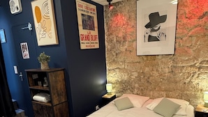 A bedroom with a bed, a nightstand, a wall clock, a poster, and a wooden bench. - Le Globe (Paris)