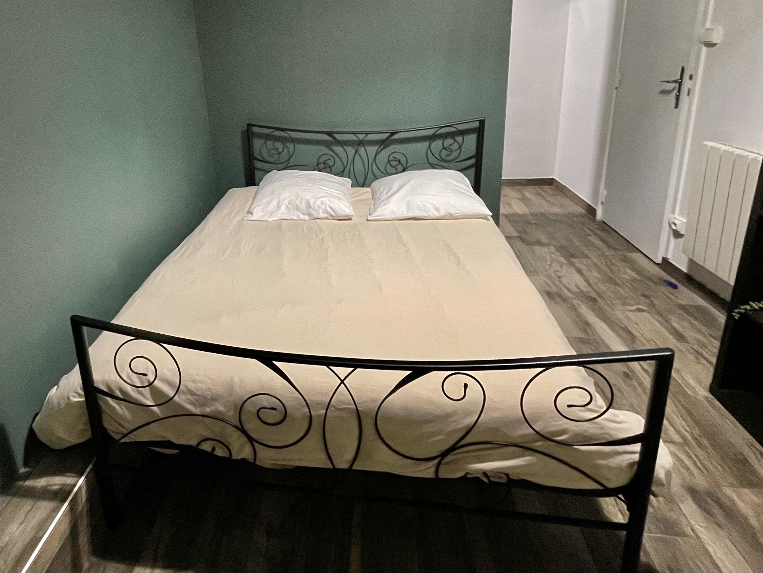 Una habitación pequeña con cama individual, cabecera de metal y una colcha sencilla.