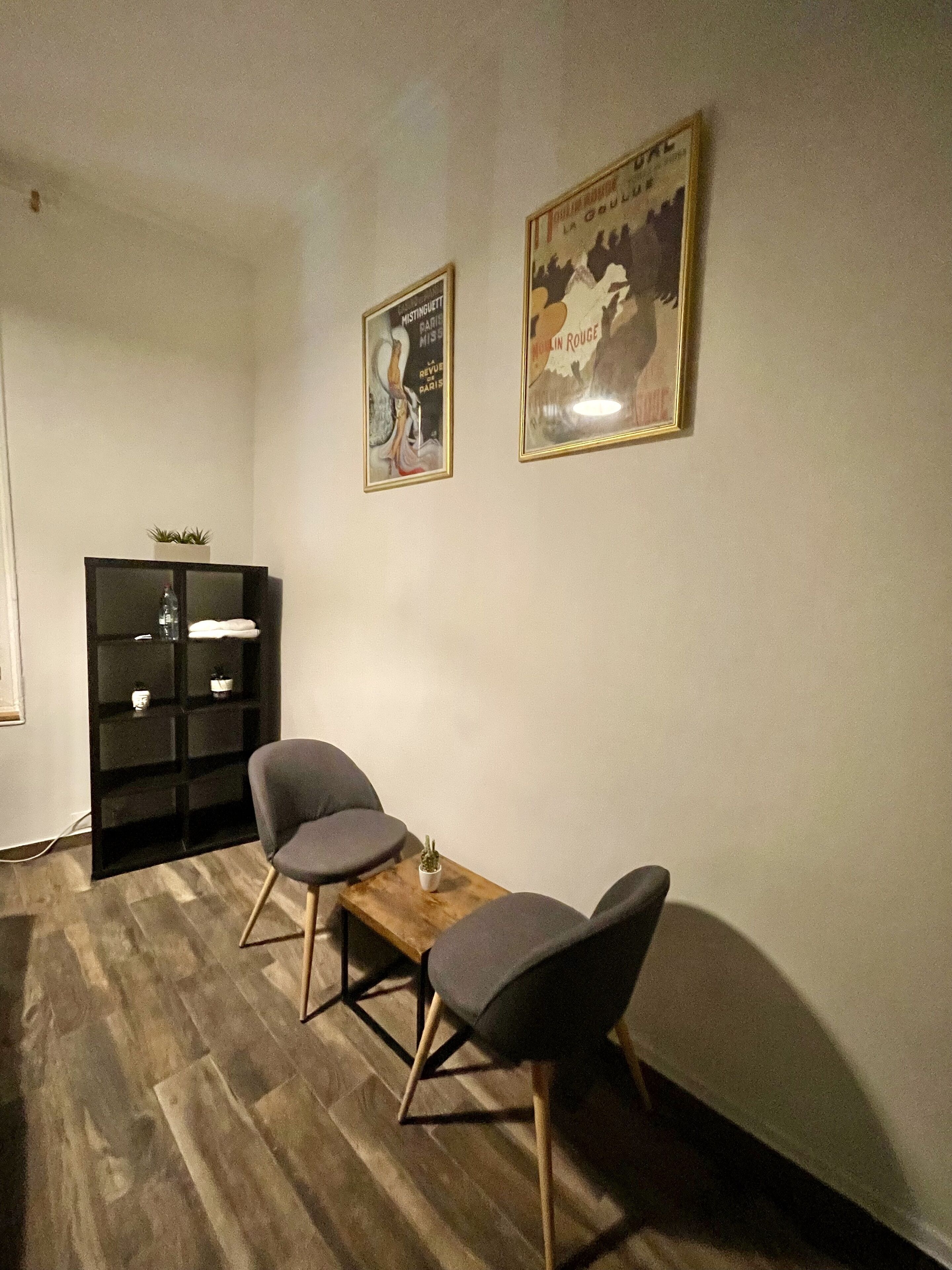 A room with two grey chairs around a wooden table, a black shelving unit, and two framed posters on the wall.