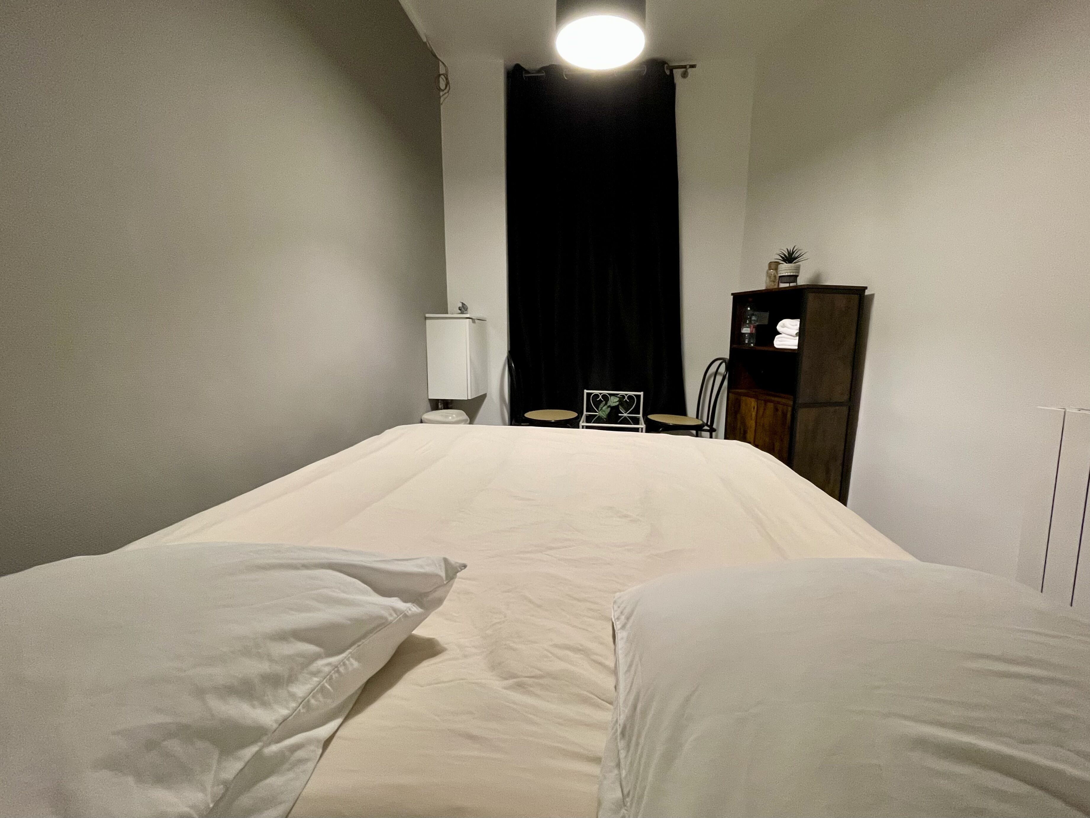 Une pièce simple et dépouillée, comprenant un lit, une petite table, une chaise, un placard et des toilettes.