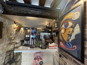 A bar area with a rustic stone wall, wooden beams, and a mural of a face. There are bar stools, a cash register, and various bottles and glasses. - Le Globe (Paris)