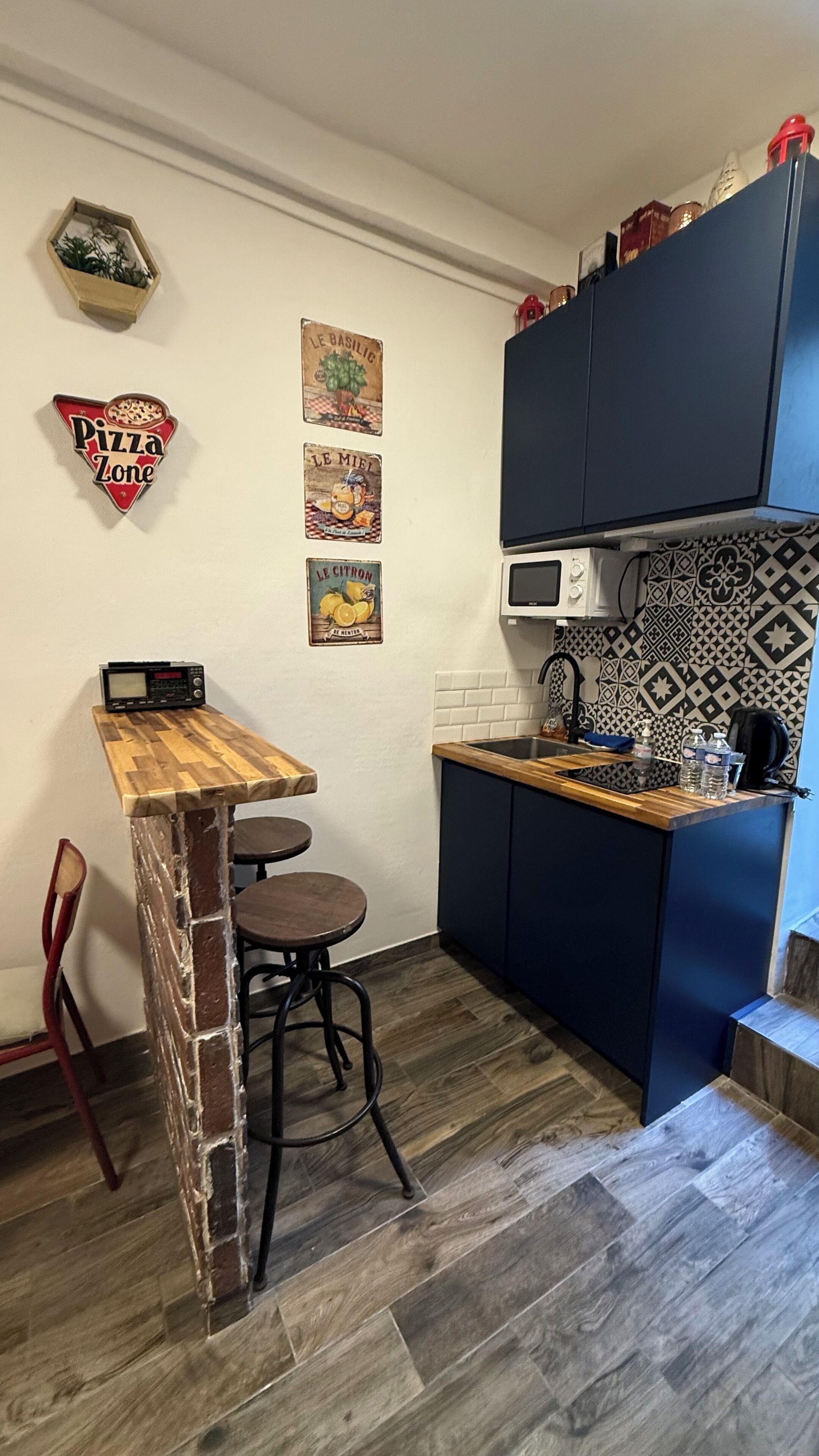 A kitchen with a wooden bar counter, a microwave, and a sink. There are stools and a brick accent wall.
