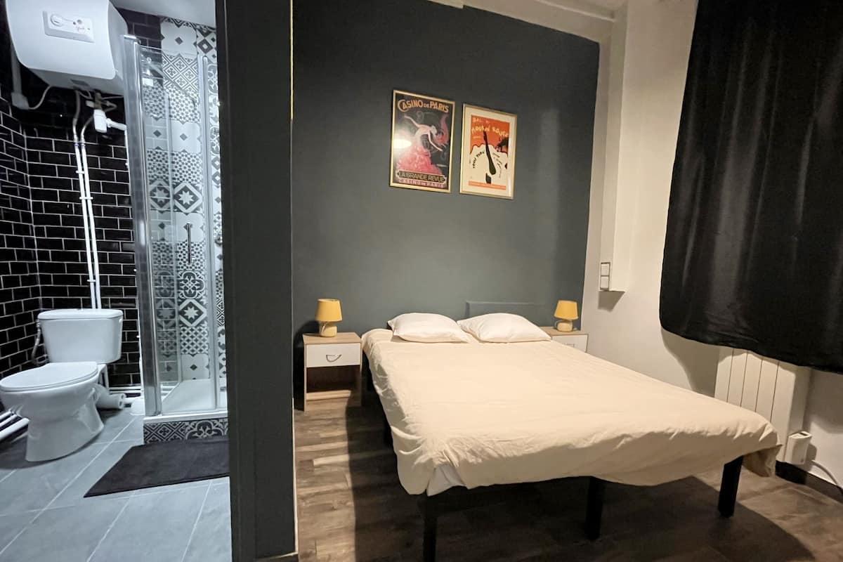 A hotel room with a bed, two bedside tables with lamps, a shower area, and a toilet.