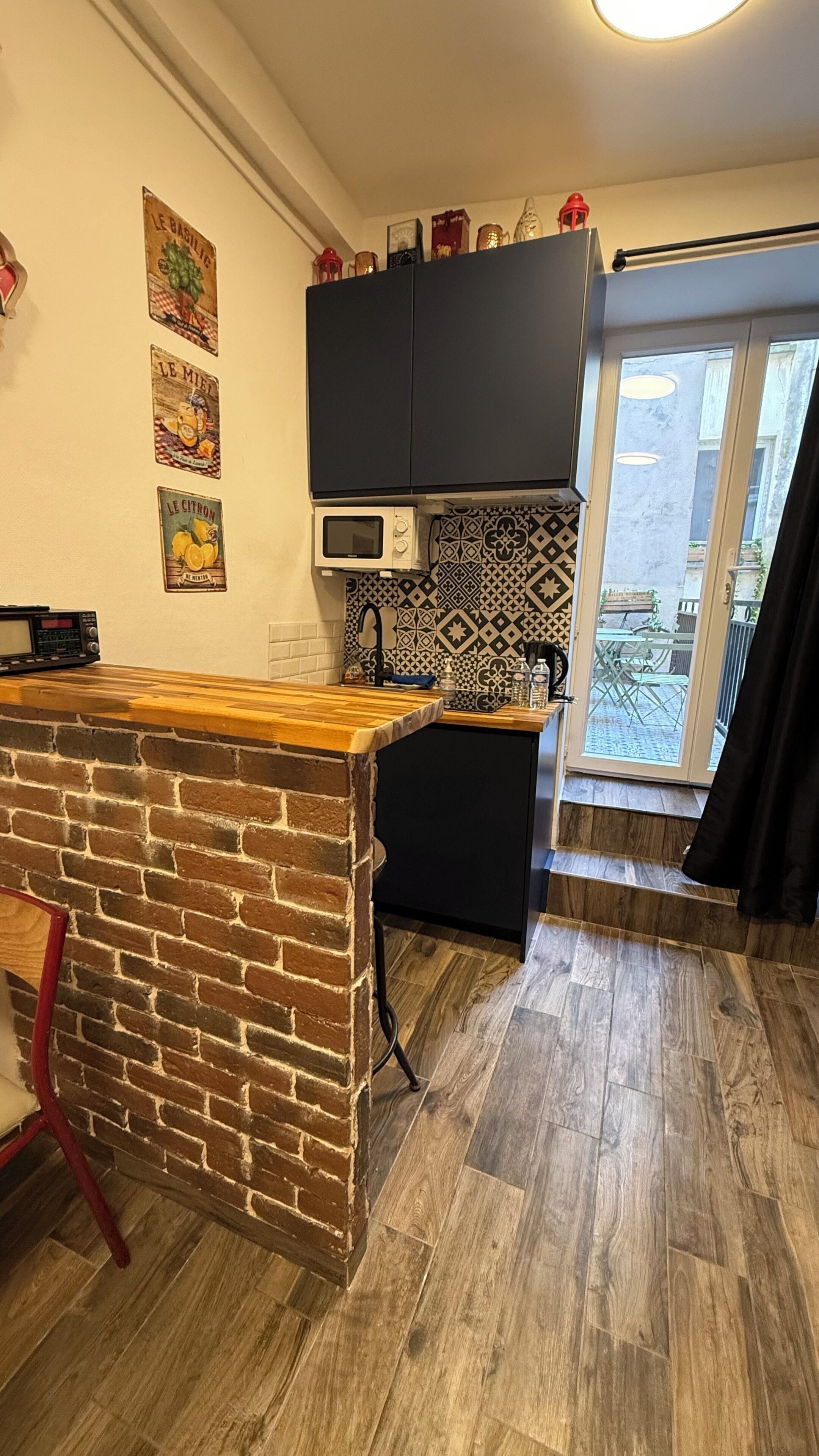 A kitchen with a brick accent wall, black cabinets, a microwave, and patterned backsplash.
