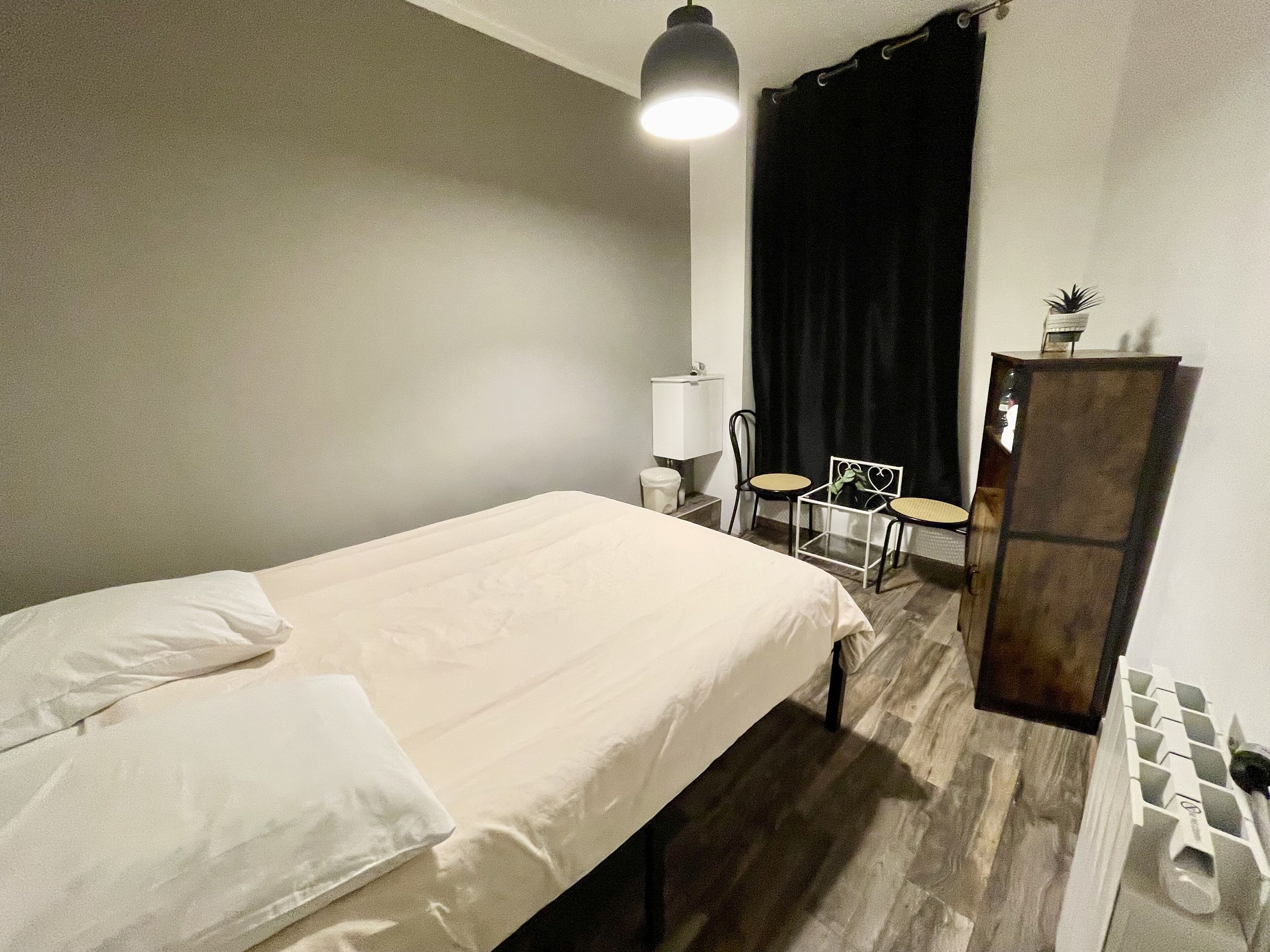 A small, neatly arranged bedroom with a single bed, a chair, a small table, a mirror, and a cabinet.