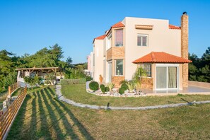 Une maison moderne à deux étages, avec un toit en tuiles, une cheminée en pierre et une pelouse bien entretenue.
