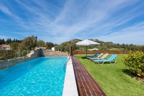 En pool med træterrasse, liggestole og et bjerg i baggrunden.