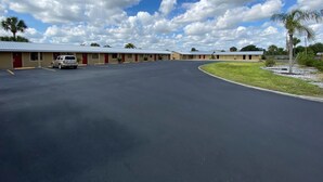 A motel with a row of single-story buildings, a parking lot, and a grassy area with palm trees. - Economy Inn (Arcadia)