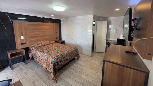 A modern bedroom with a wooden bed, a desk, a mirror, and a bathroom door. - Economy Inn (Arcadia)