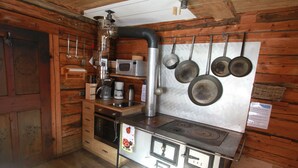A rustic kitchen with wooden walls, a stove, and hanging pots. - Ferienwohnungen am Berg - Almhütte Alfen (Innervillgraten)