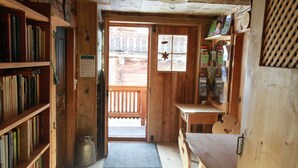 A wooden interior with a door leading outside, a bookshelf, a small table, and a window with a star decoration. - Ferienwohnungen am Berg - Almhütte Alfen (Innervillgraten)