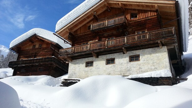 A wooden chalet with multiple balconies and a snow-covered roof, surrounded by snow. - Ferienwohnungen am Berg - Almhütte Alfen (Innervillgraten)