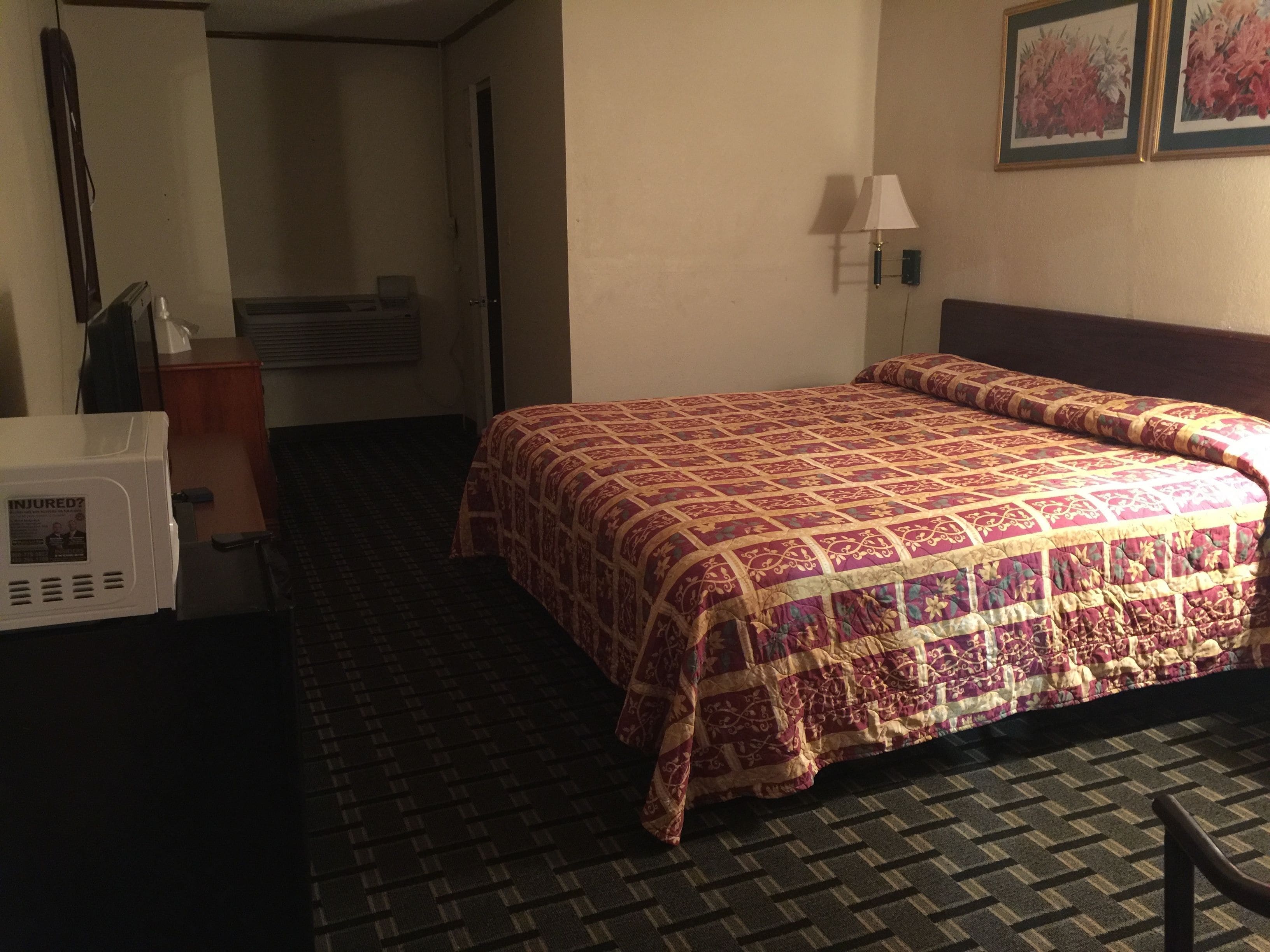 A hotel room with a bed, a desk, a lamp, and a wall-mounted picture.