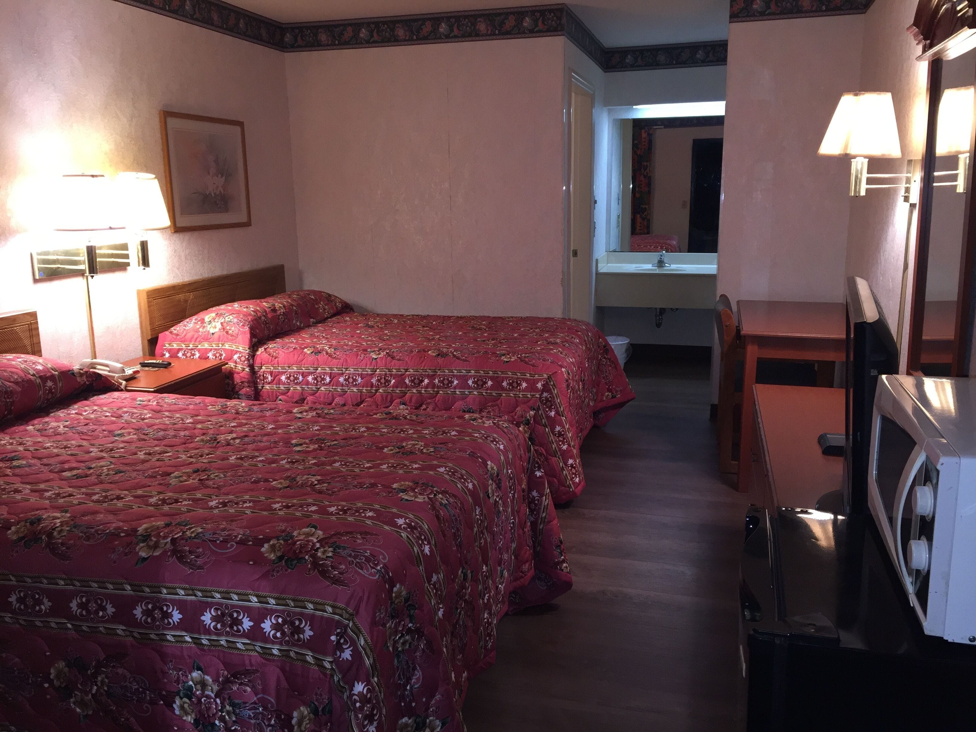 A hotel room with two beds, a desk, a television, and a bathroom visible through an open door.