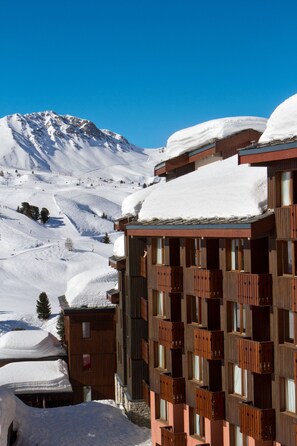 A snow-covered mountain with a wooden building featuring balconies and windows. - Belambra Hotels & Resorts Cassiopee (La Plagne-Tarentaise)