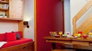 A cozy room with a wooden staircase, a red sofa, a wooden table with breakfast items, and a bookshelf.
