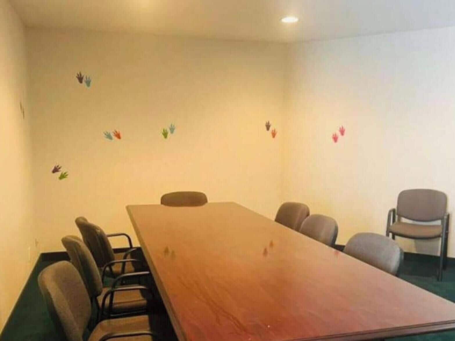 A conference room with a long table, six chairs, and handprint decorations on the walls.