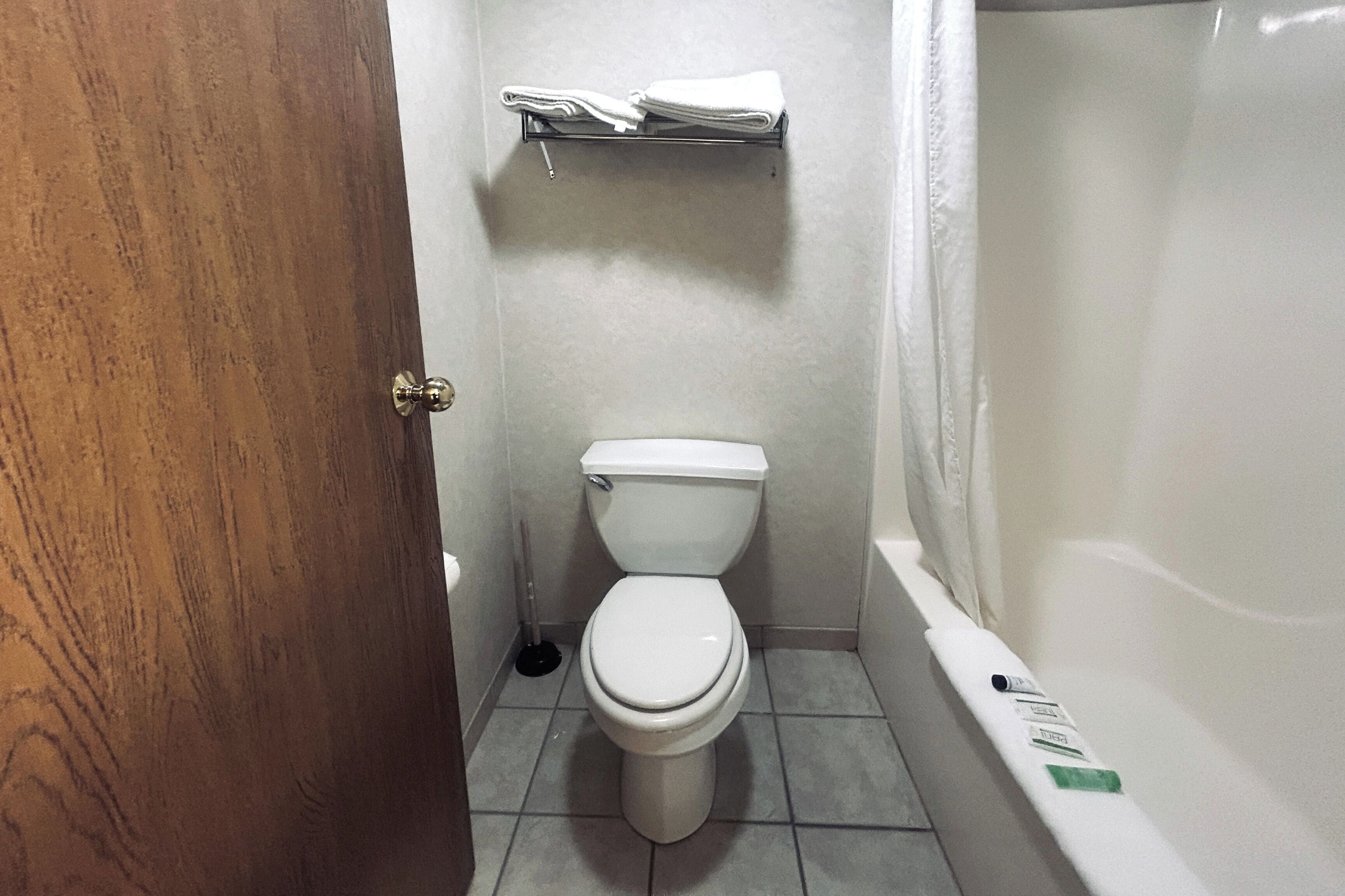 A bathroom with a toilet, a shelf with folded towels, and a bathtub.