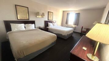 A hotel room with two beds, a desk, a lamp, and framed pictures on the walls.