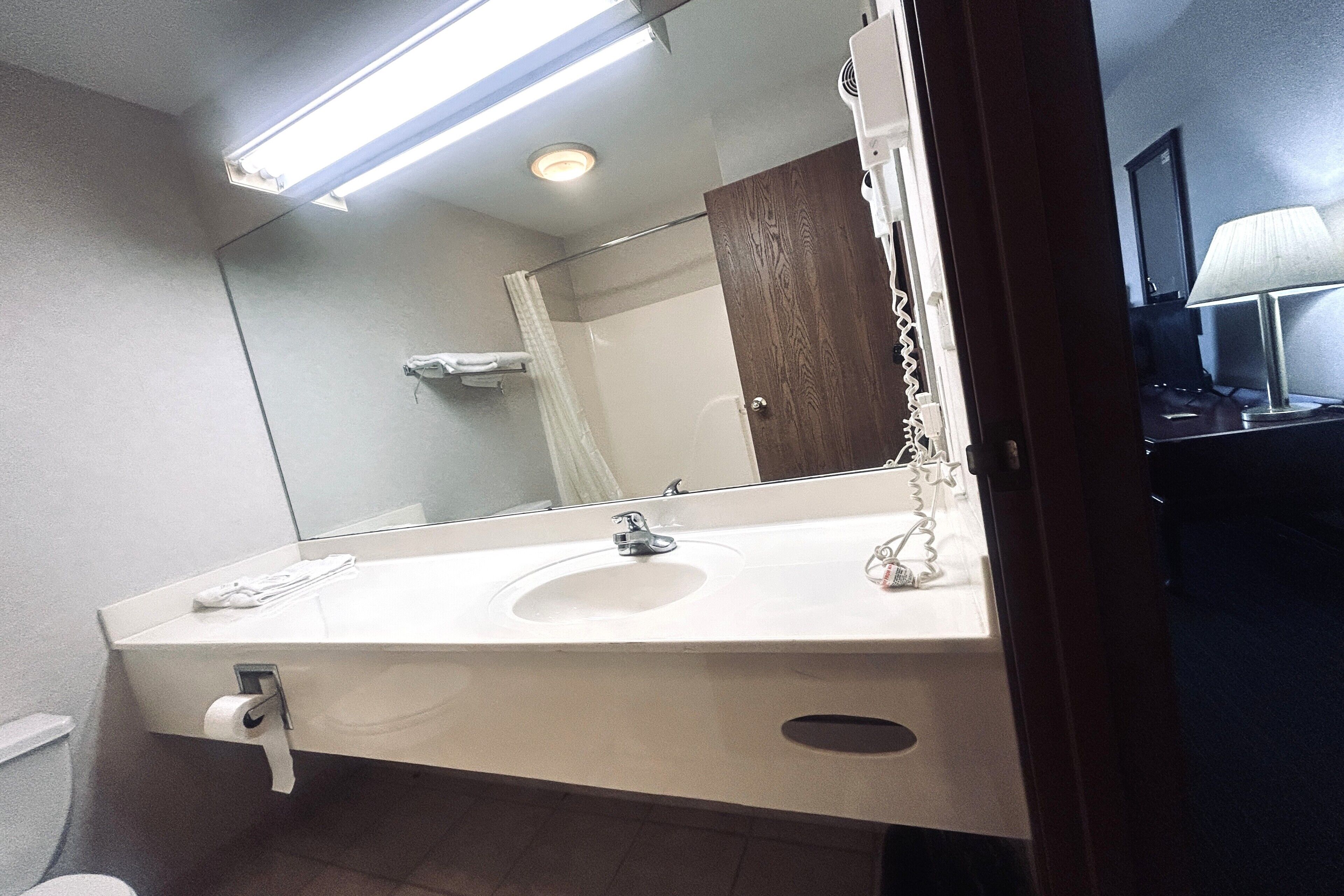 Un baño con lavamanos blanco, un espejo, cortina de ducha y un perchero.