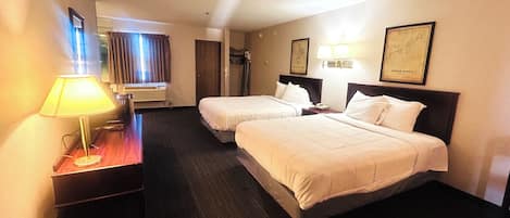Ein Hotelzimmer mit zwei Betten, einem Schreibtisch mit Lampe, einer Klimaanlage und gerahmten Bildern an der Wand.