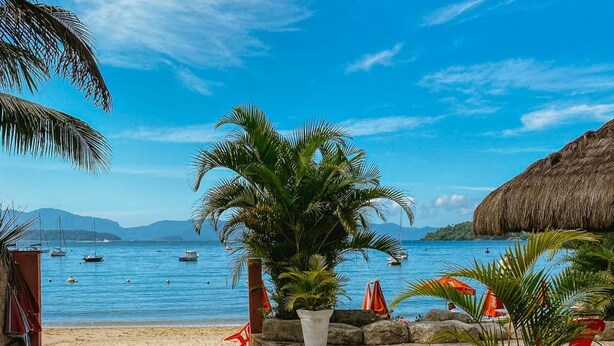 A beachside patio with a view of the sea, potted plants, and a thatched-roof structure. - Pousada Angra Bella (Angra dos Reis)