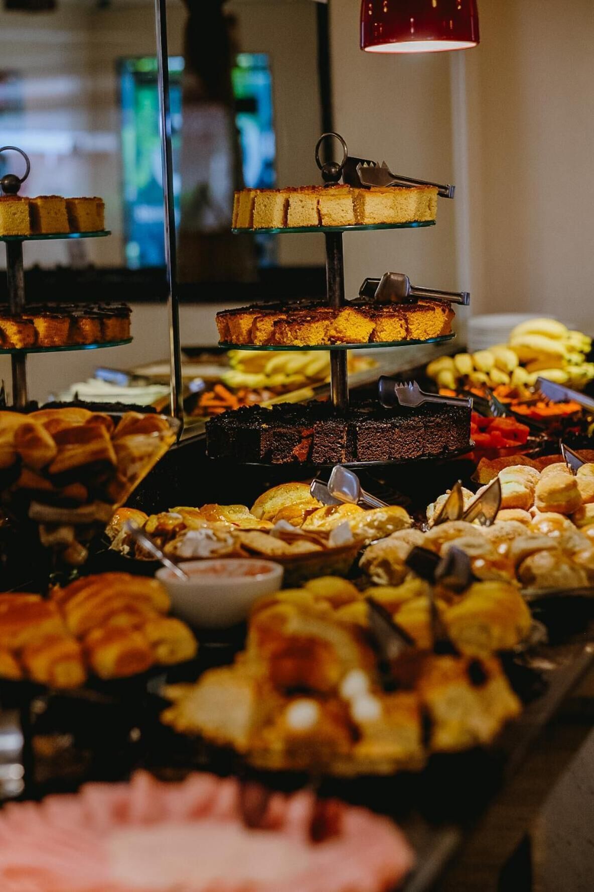 Buffet com diversos doces e pastelaria, incluindo bolos e tortas, disposto em uma vitrine de vidro.