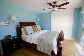 A bedroom with a bed, nightstand, wall sconces, ceiling fan, and a window with blinds. - Luxury Oceanfront Estate (Pompano Beach)