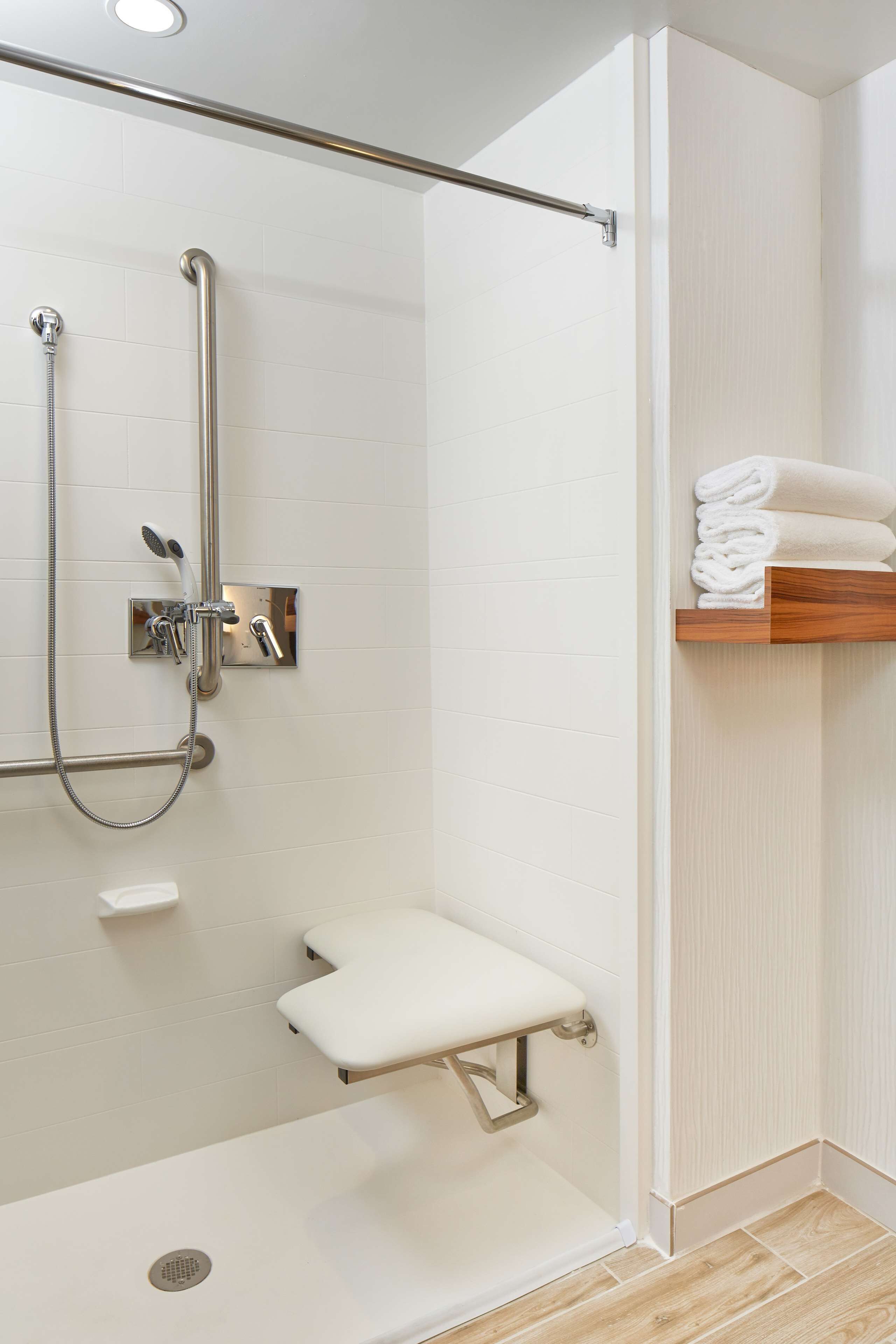 Un baño moderno con ducha a nivel, inodoro con barra de apoyo y estante con toallas dobladas.