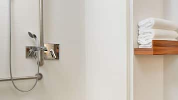 Un baño moderno con ducha a nivel, inodoro con barra de apoyo y estante con toallas dobladas.